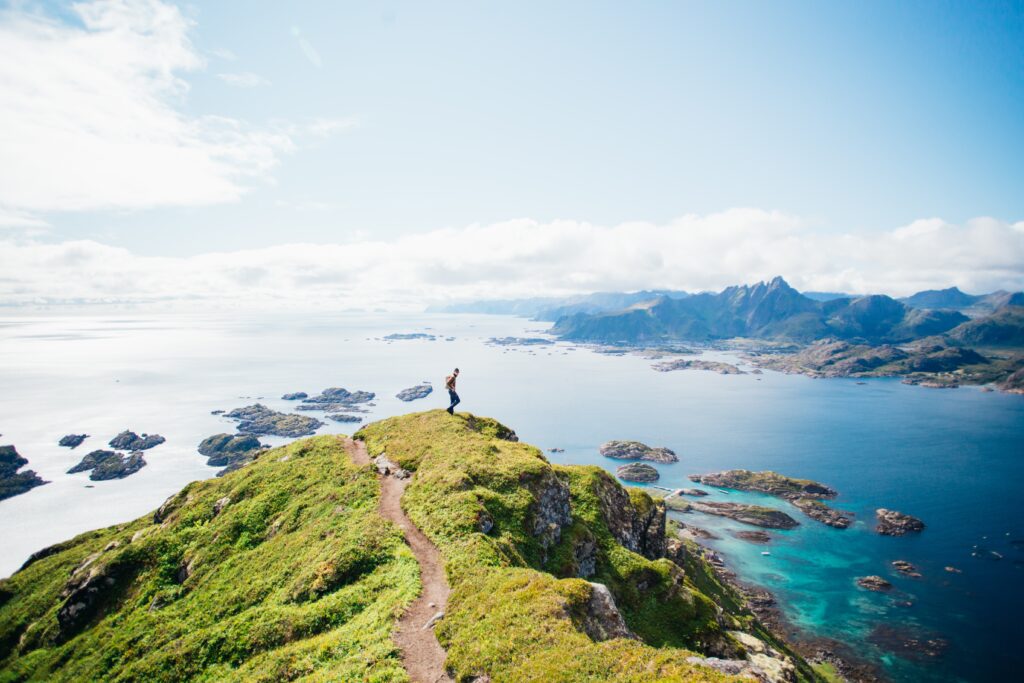 Christoffel Travel – avontuurlijke reiziger op bergtop met uitzicht over de blauwe oceaan tijdens een zonnige dag.